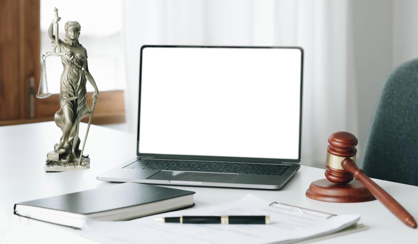 area di lavoro dell'avvocato con schermo bianco vuoto del computer portatile e martello di legno della legge e scala del giudice in ottone. concetto legale di aula di tribunale. foto