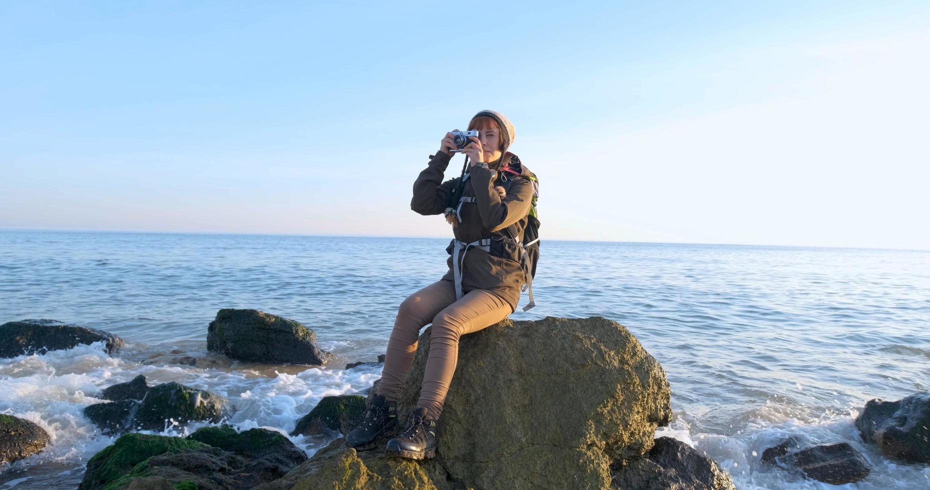 giovane viaggiatore femminile con zaino e fotocamera a pellicola retrò viaggia nelle montagne autunnali vicino al mare foto