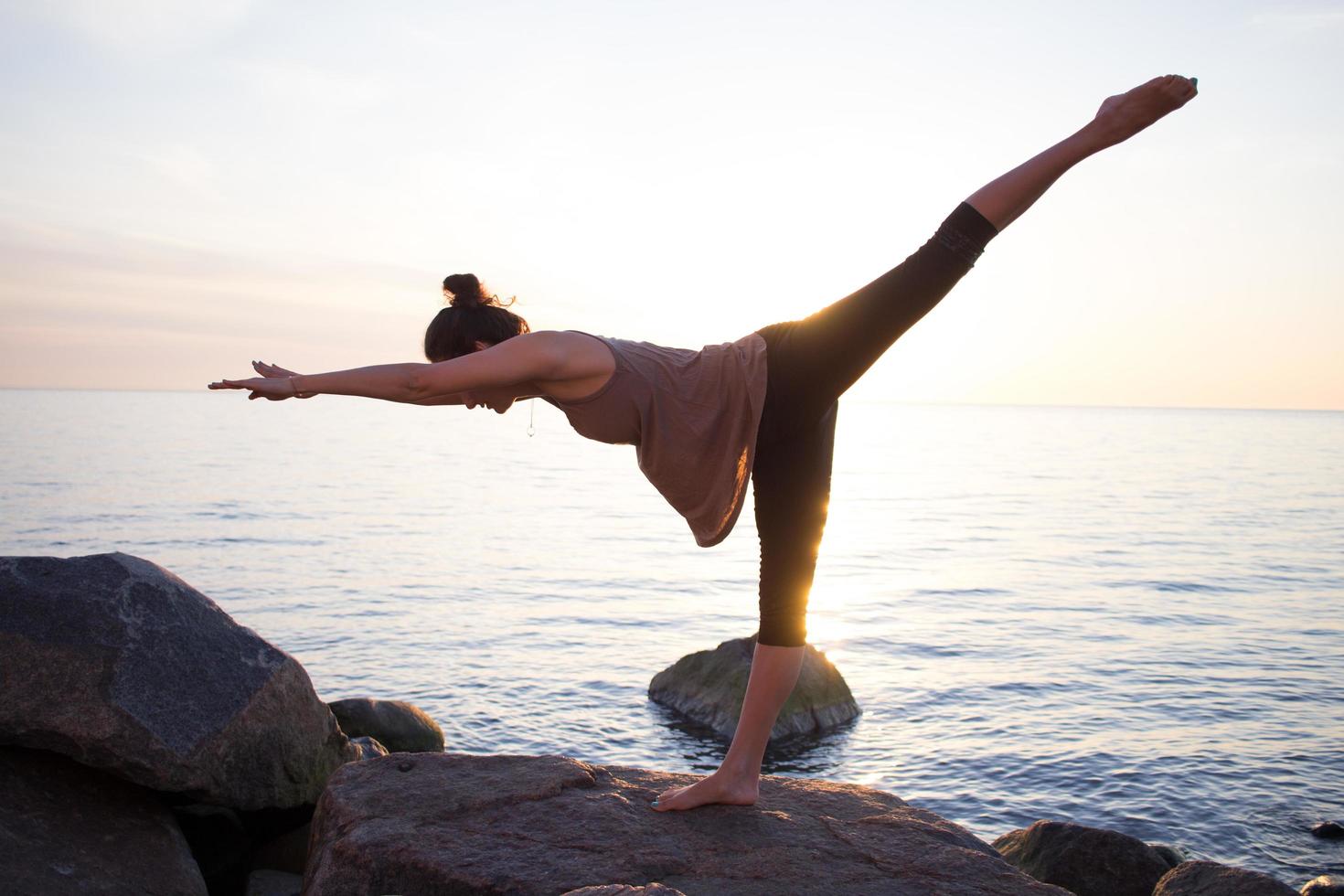 fitness razza mista donna asiatica in posa yoga sulla spiaggia del mattino, bella donna in forma pratica fitness exrxise pietre, mare mattutino o sfondo oceano foto