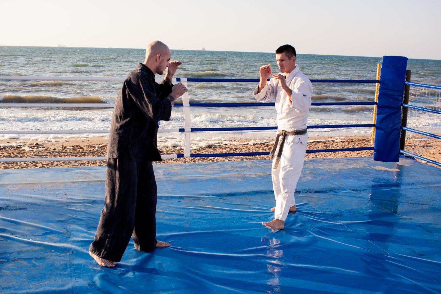 combattenti di karate stanno combattendo sul ring di pugilato della spiaggia al mattino foto