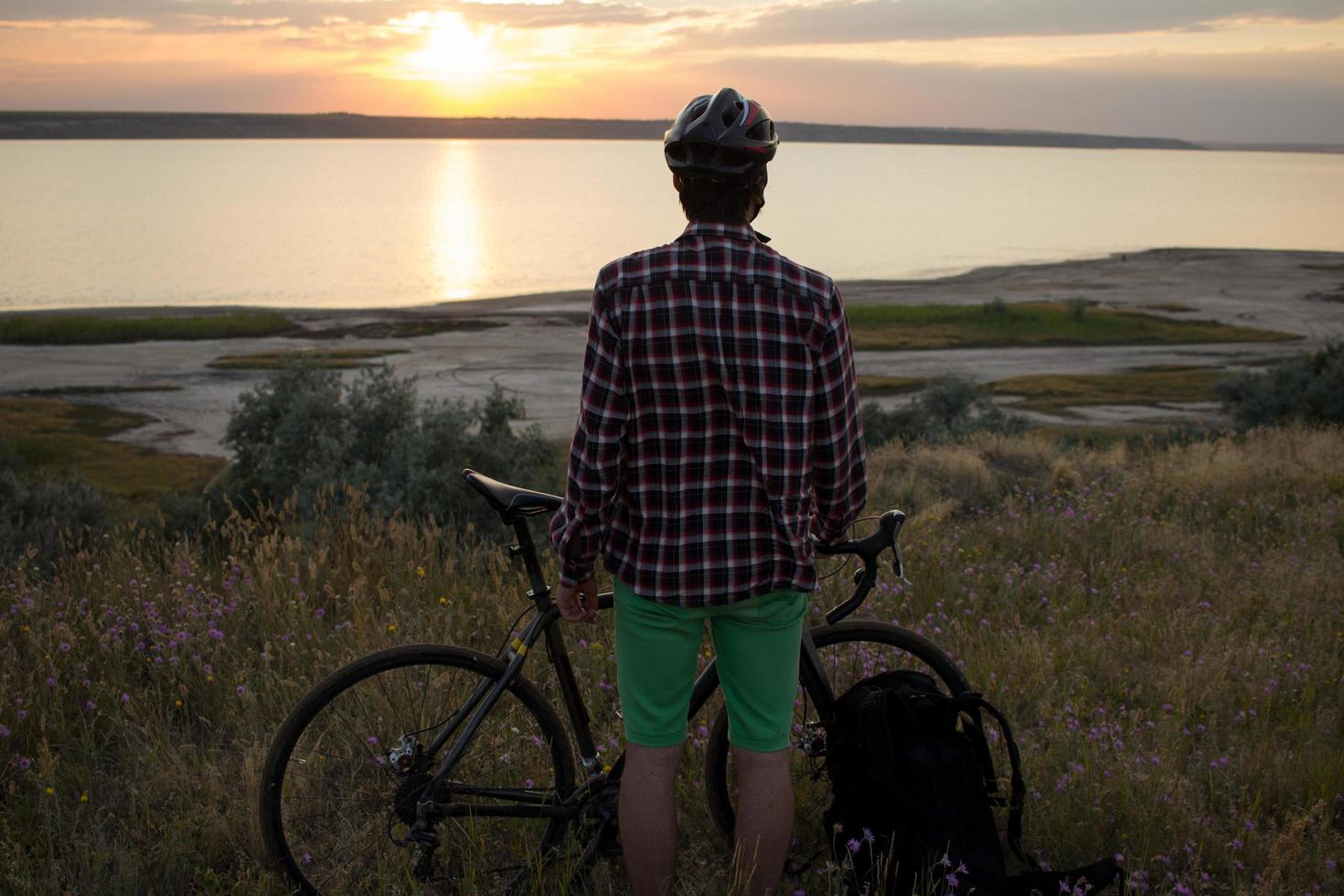 silhouette di un uomo con bici da strada da turismo che guarda e fa foto del tramonto nel lago sul cellulare