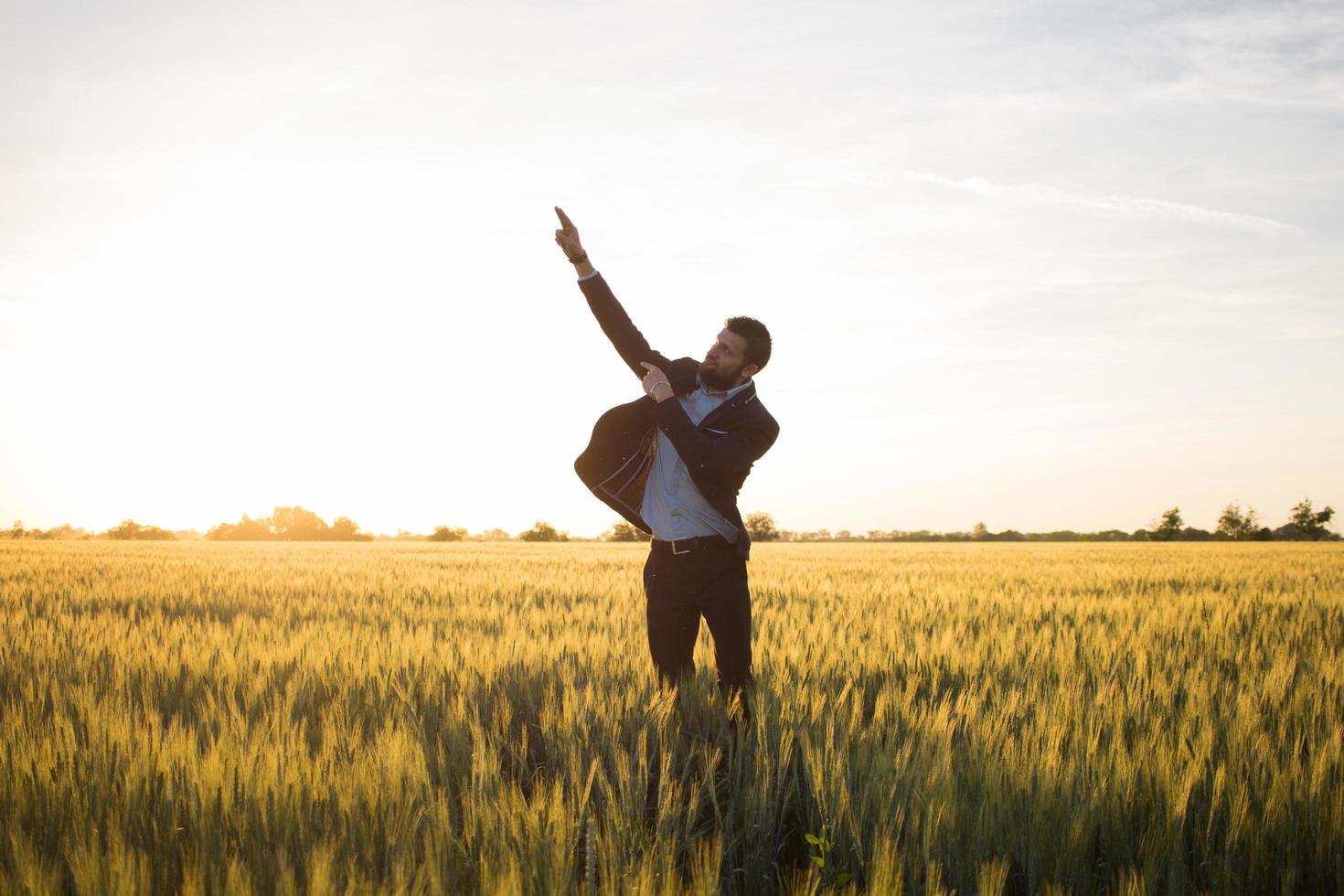 concetto di vincitore, felice giovane imprenditore salta con le mani alzate nei campi, piante di grano estivo foto