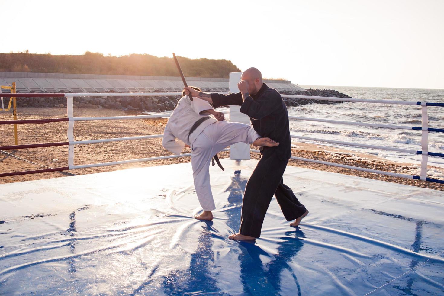 combattenti di karate stanno combattendo sul ring di pugilato della spiaggia al mattino foto