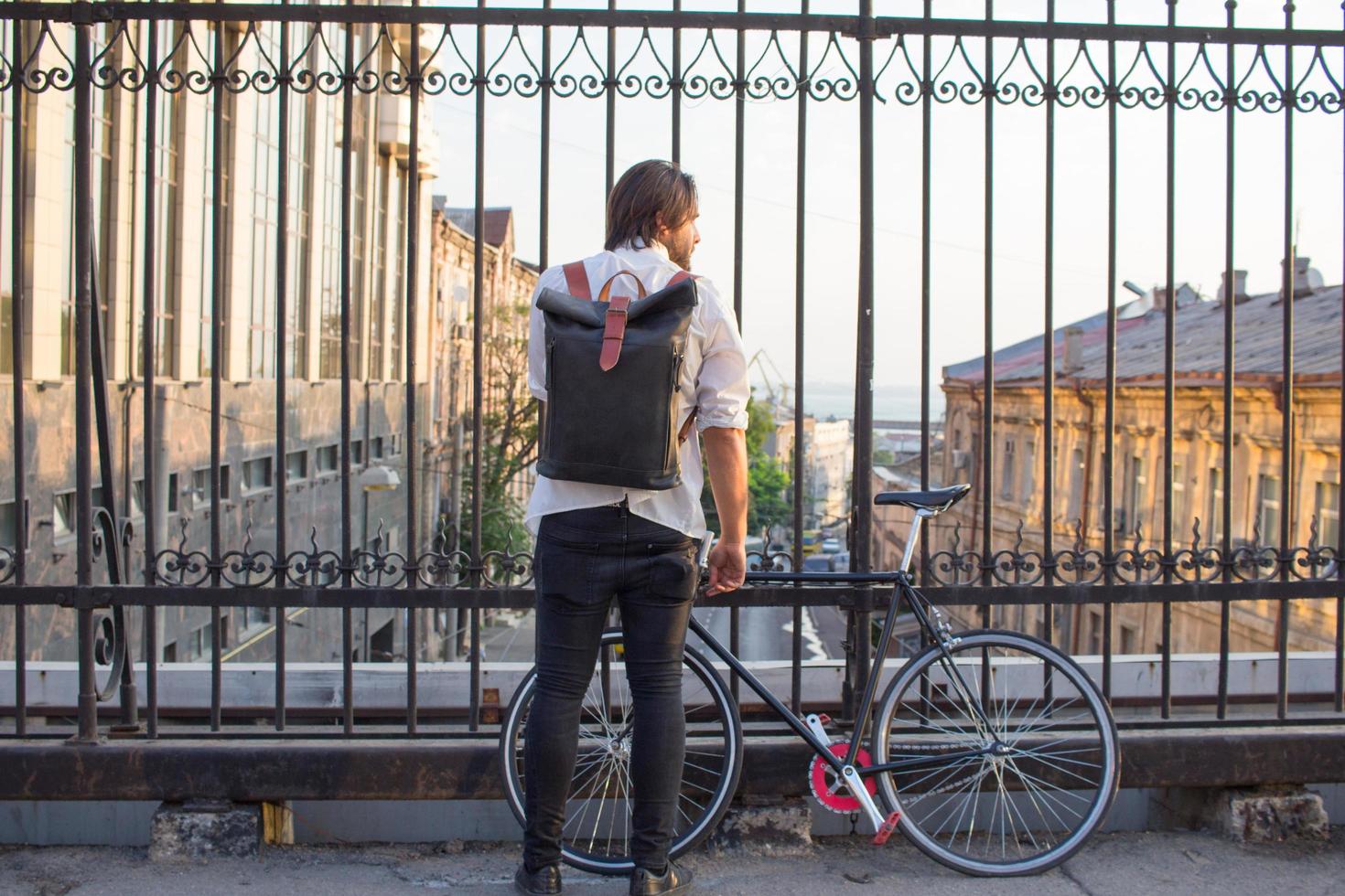 giovane uomo barbuto con zaino in pelle che cammina con la bicicletta nera foto