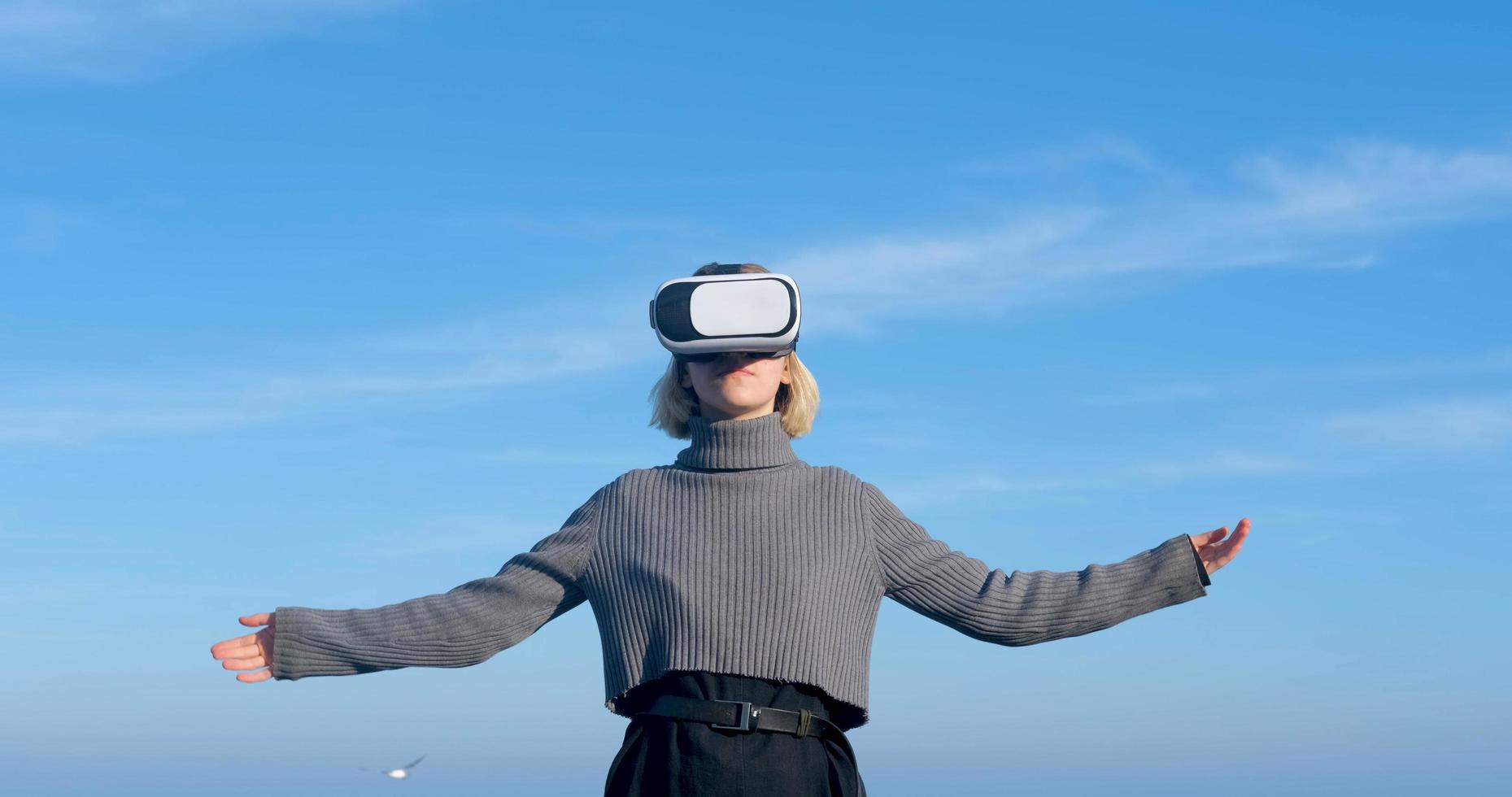 giovane donna bella con occhiali per realtà virtuale all'aperto sulla spiaggia contro il cielo blu soleggiato foto