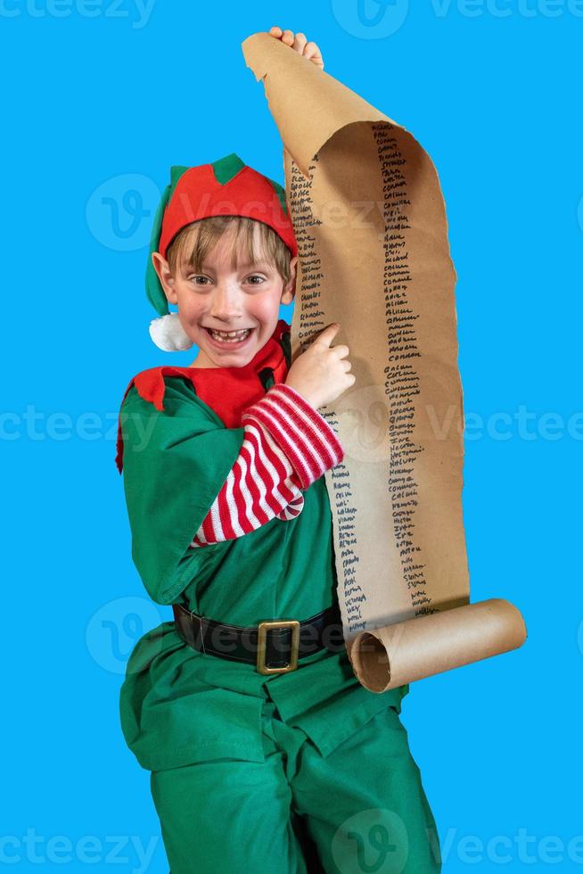 ragazzo felice vestito da elfo di natale che punta alla lista di babbo natale su sfondo blu foto