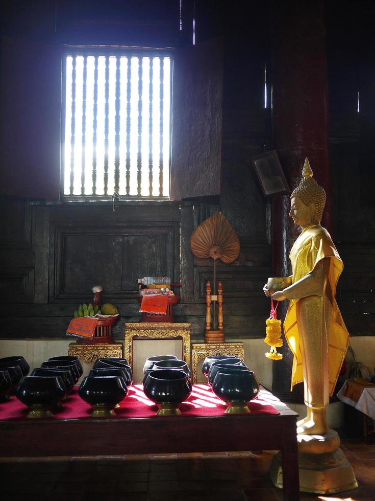 Buddha d'oro in piedi nel vecchio tempio di legno con un sacco di ciotola per l'elemosina foto