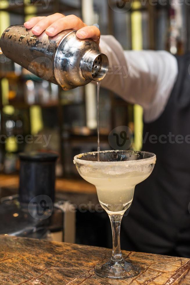 barman al lavoro, preparare cocktail. versando la margarita nel bicchiere da cocktail. foto