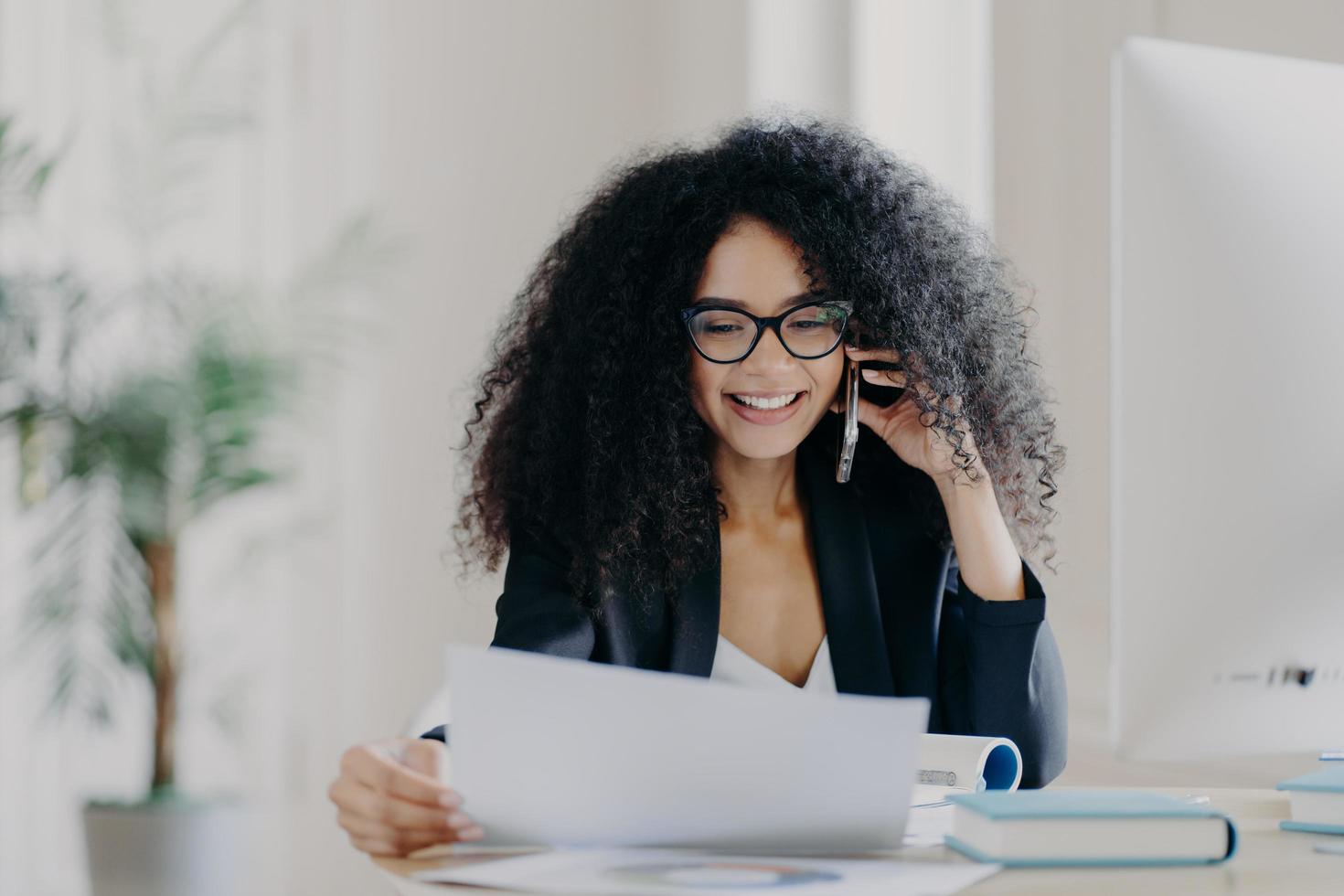 amministratore delegato donna esperta ha conversazioni telefoniche, risolve problemi, si concentra sui documenti, indossa occhiali e abiti formali, posa sul posto di lavoro, ha un'espressione allegra. direttore amministrativo foto