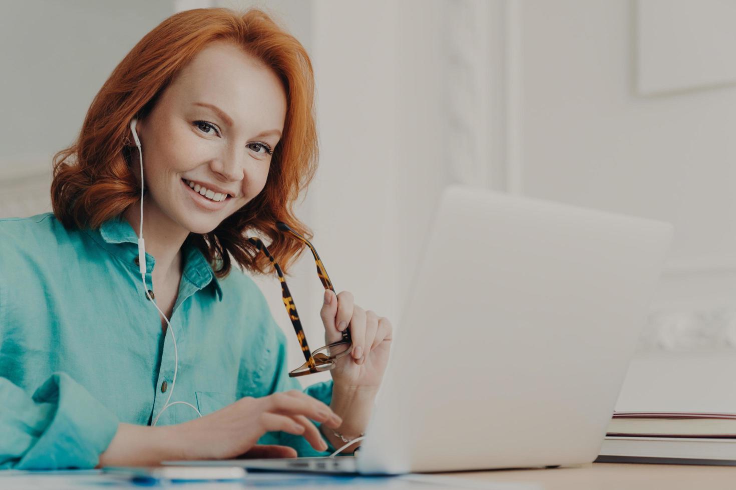 sorridente bella dipendente femminile parla in videochiamata, ha una conferenza web con i colleghi, guarda webinar su laptop moderno, posa nello spazio di coworking. lo studente impara le lingue straniere online foto