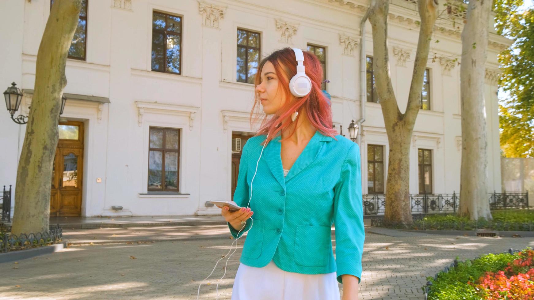 giovane donna con abito colorato e capelli rosa beve caffè e ascolta musica nel parco foto