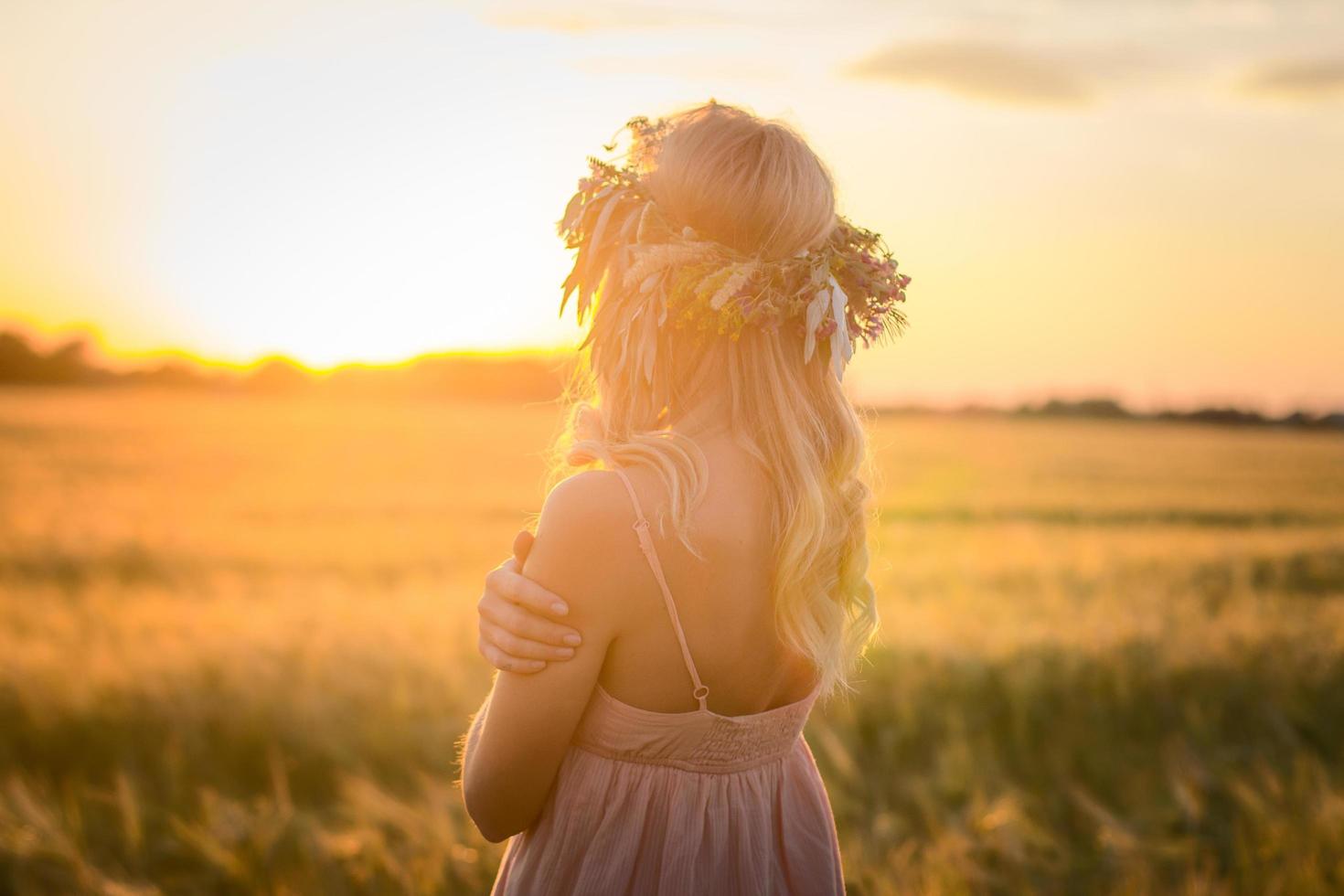 ritratti di giovane donna che si diverte nel campo di grano durante il tramonto, signora in testa corona di fiori durante foto