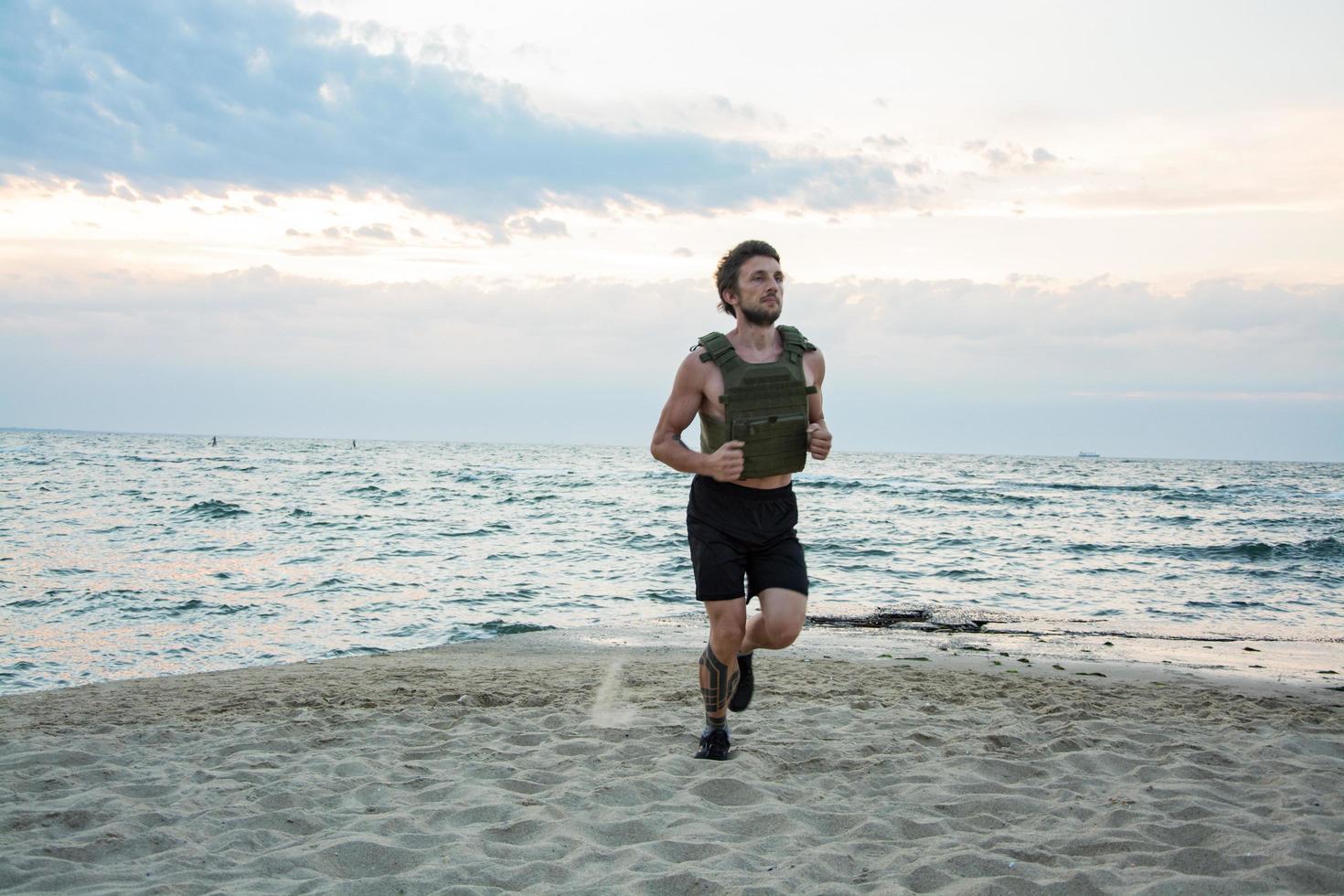 giovane atleta barbuto che si allena all'aperto con giubbotto zavorrato, esercizio con portatarga militare foto