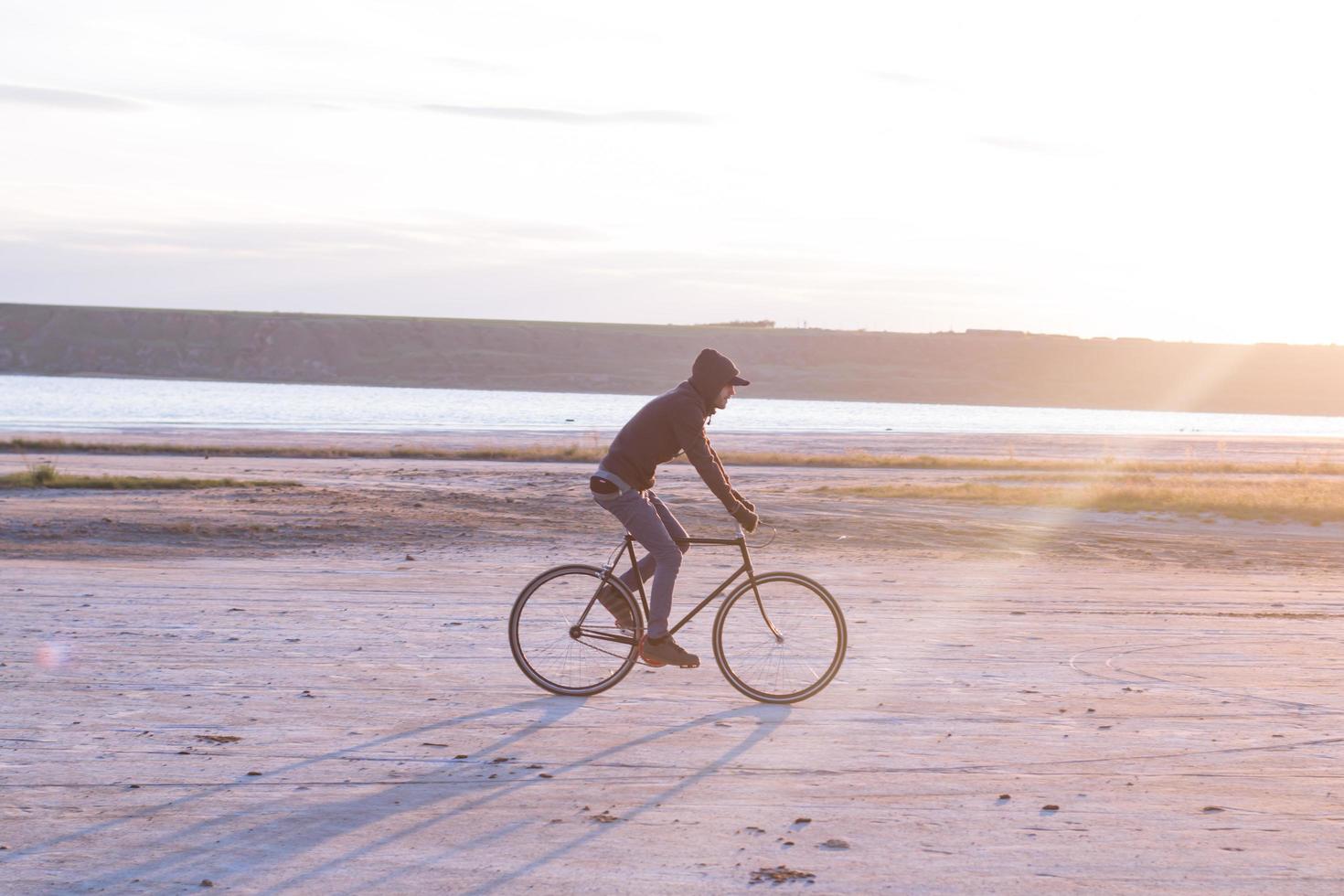 pilota da solo su bici da strada a scatto fisso che guida nel deserto vicino al fiume, foto di ciclista turistico hipster.