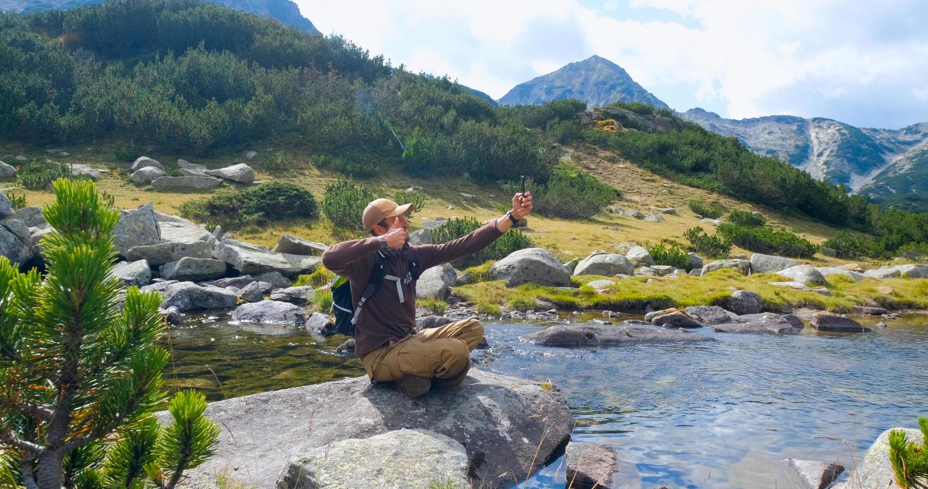 yong viaggiatore maschio in montagna seduto vicino al fiume foto