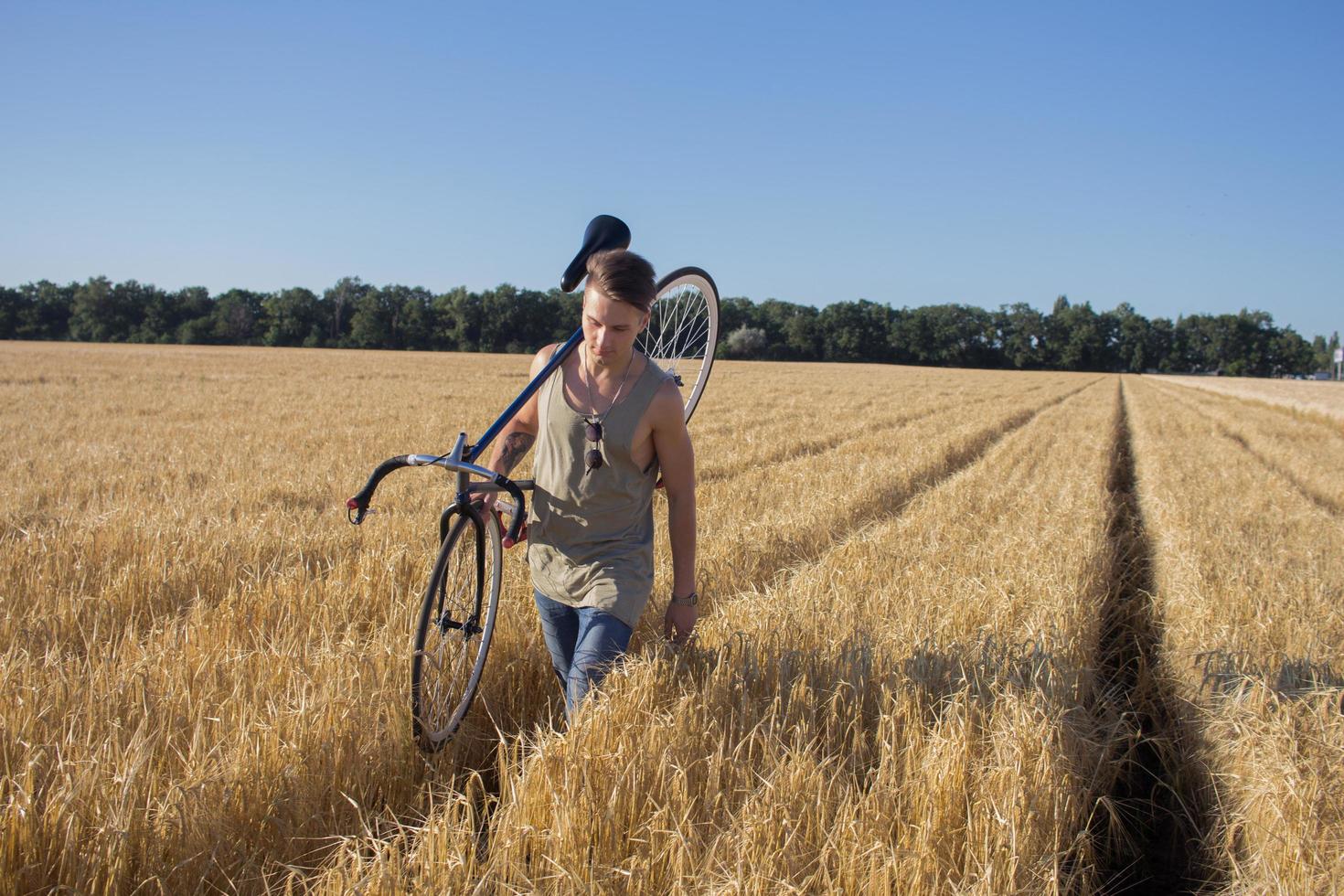 il giovane guida la bici a scatto fisso sulla strada di campagna, sui campi e sullo sfondo del cielo blu foto