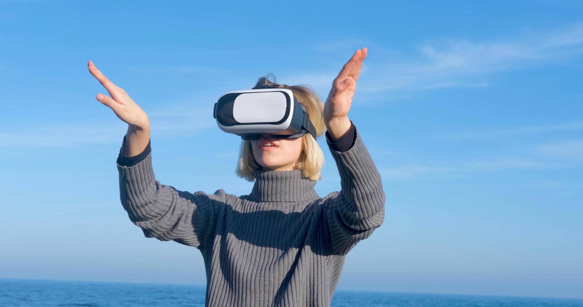giovane donna bella con occhiali per realtà virtuale all'aperto sulla spiaggia contro il cielo blu soleggiato foto