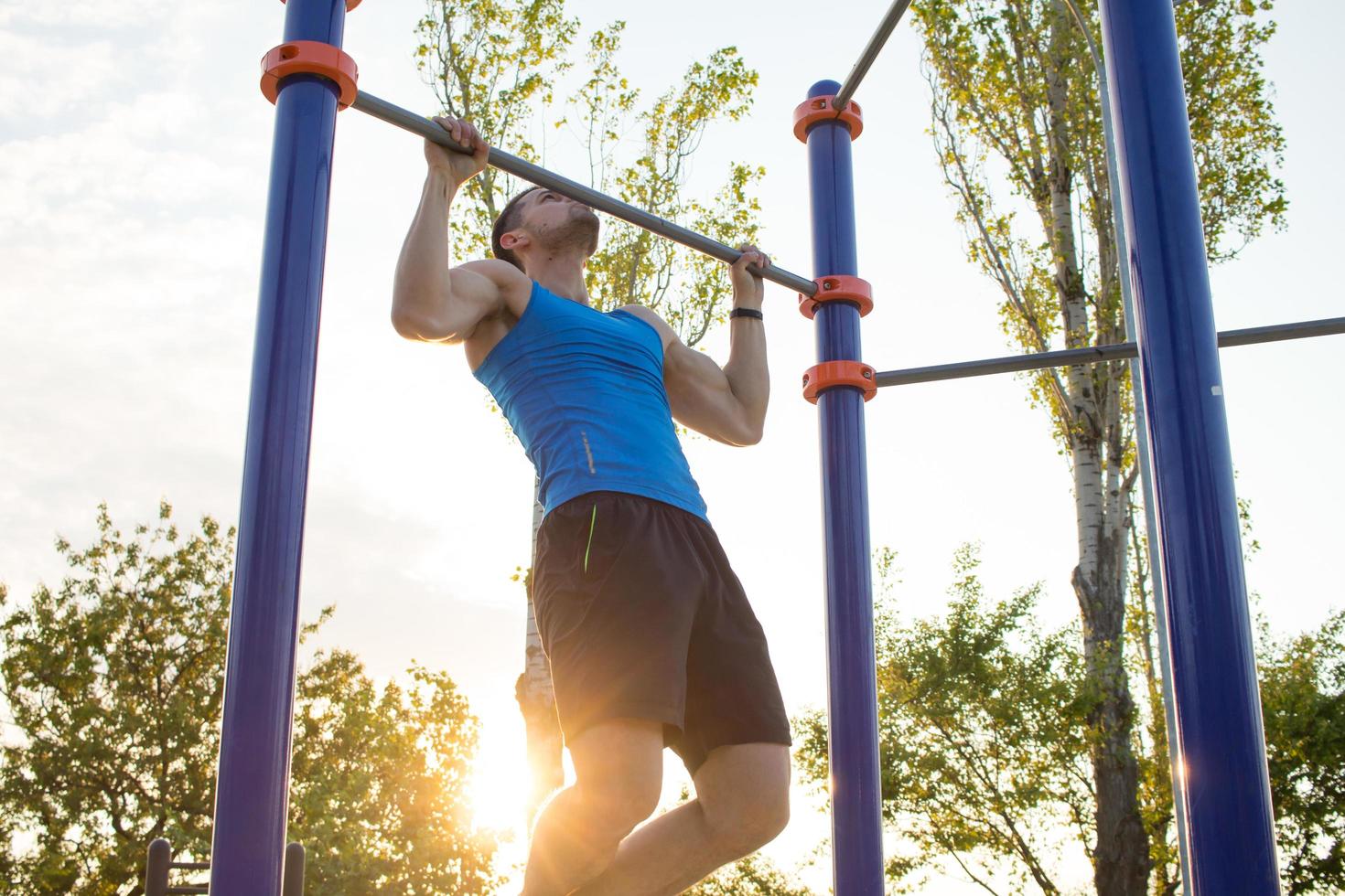 uomo muscoloso che fa pull-up sulla barra orizzontale, allenamento di strongman sulla palestra del parco all'aperto al mattino. foto