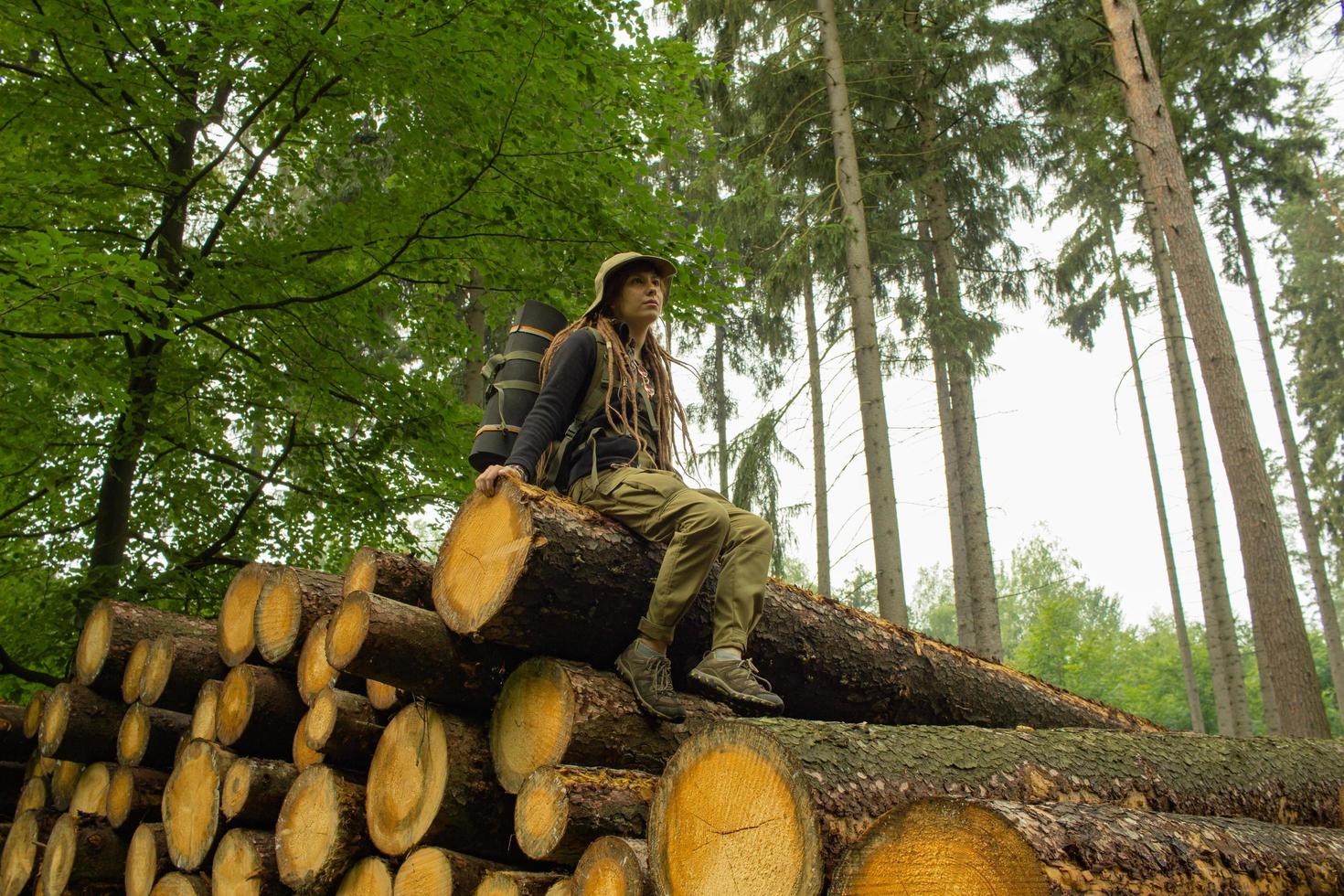 giovane escursionista femminile in posa vicino alla farina di sega nella foresta di pini. molti tronchi d'albero nella foresta. viaggiatore zaino in spalla donna. foto