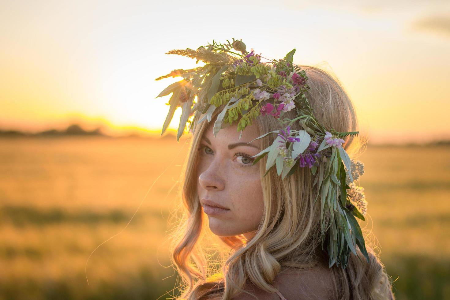 ritratti di giovane donna che si diverte nel campo di grano durante il tramonto, signora in testa corona di fiori durante foto