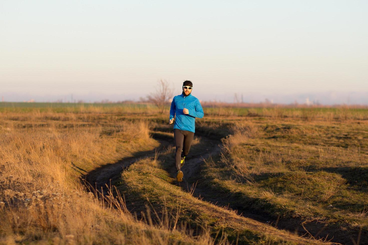 giovane trail runner che si allena all'aperto nei campi, tramonto sullo sfondo del lago foto