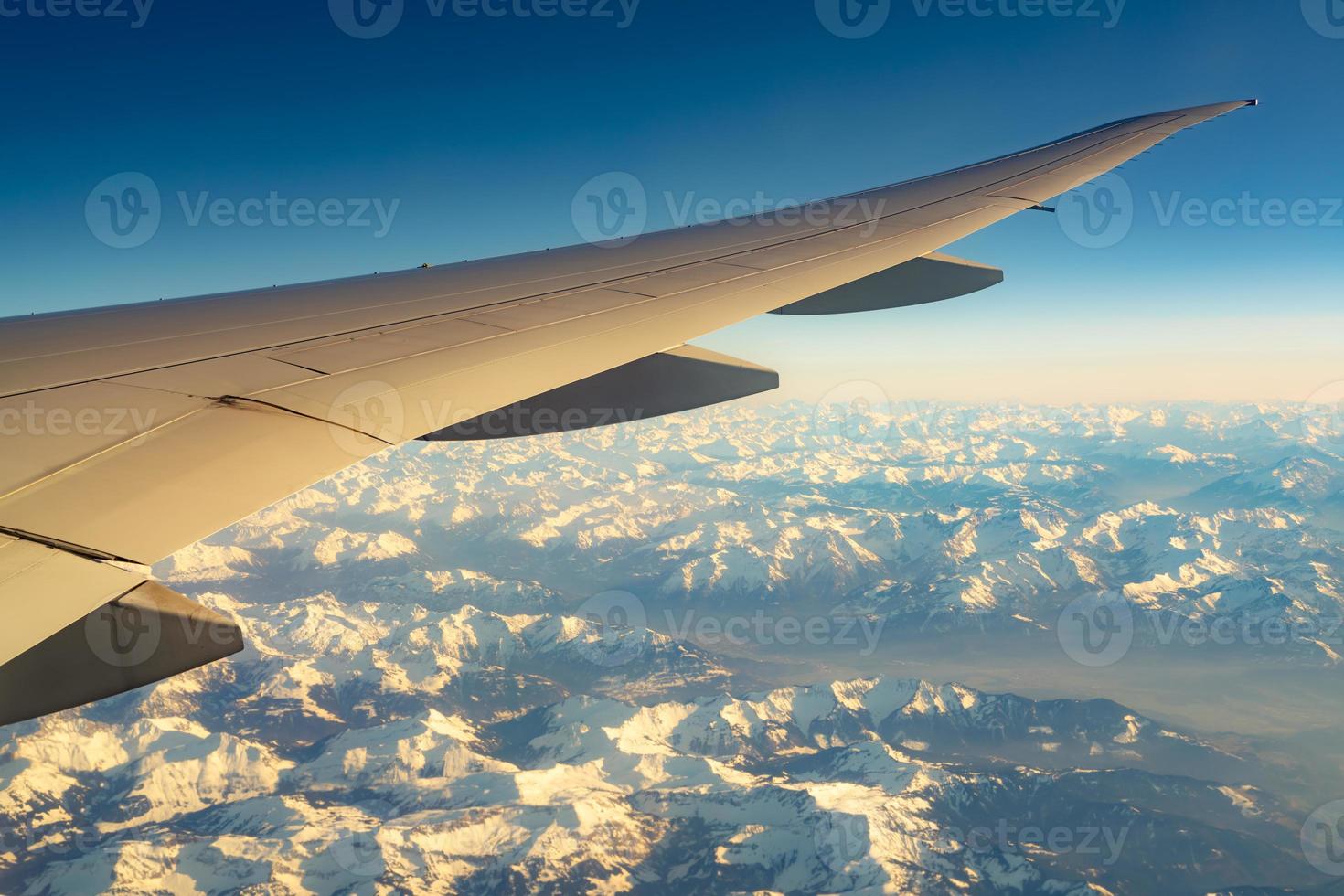 ala dell'aereo sopra la copertura della montagna con neve bianca. aereo che vola sul cielo blu. vista panoramica dalla finestra dell'aeroplano. volo di una compagnia aerea commerciale. ala dell'aereo. concetto di meccanica di volo. volo internazionale. foto