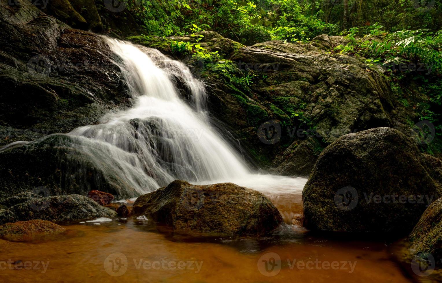 bellissima cascata nella giungla. cascata nella foresta tropicale con albero verde e luce solare. la cascata scorre nella giungla. sfondo della natura. roccia o pietra a cascata. viaggio nella stagione verde in Thailandia foto