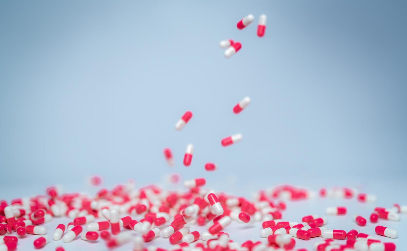 il fuoco selettivo sulla pillola della capsula rosa-bianca cade sul tavolo bianco. uso di farmaci antibiotici con ragionevole. resistenza ai farmaci antibiotici. industria farmaceutica. mercato dei farmaci antimicrobici. foto