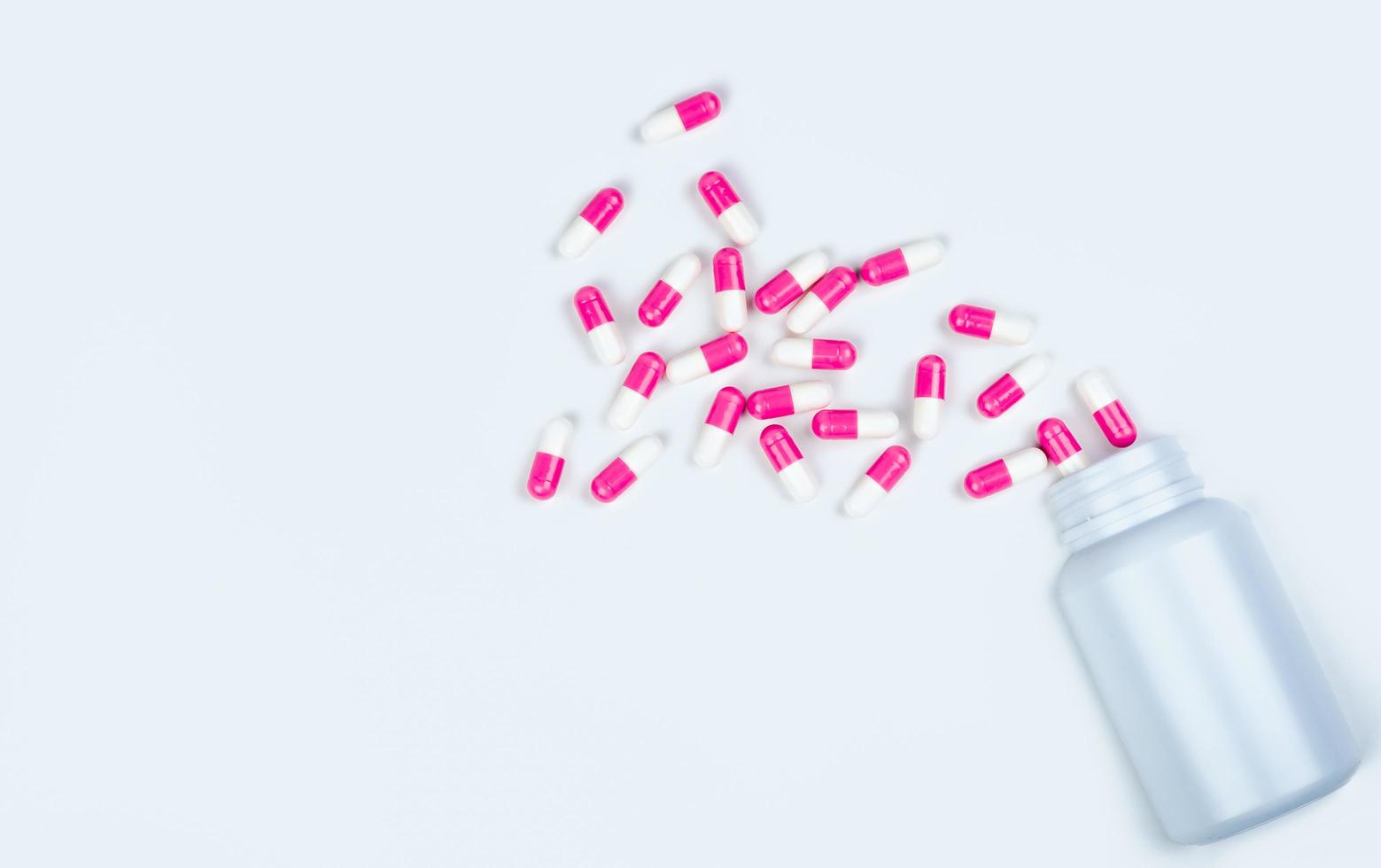 pillole di capsule rosa-bianche sparse dal flacone di droga. farmaco antipsicotico. capsule medicinali per il trattamento della depressione. farmaco ansiogeno. assistenza sanitaria globale. sfondo della farmacia. industria farmaceutica. foto