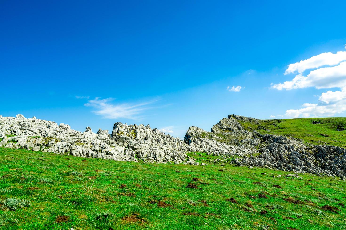 paesaggio di erba verde e collina rocciosa in primavera con un bel cielo azzurro e nuvole bianche. vista campagna o campagna. sfondo della natura in una giornata di sole. foto