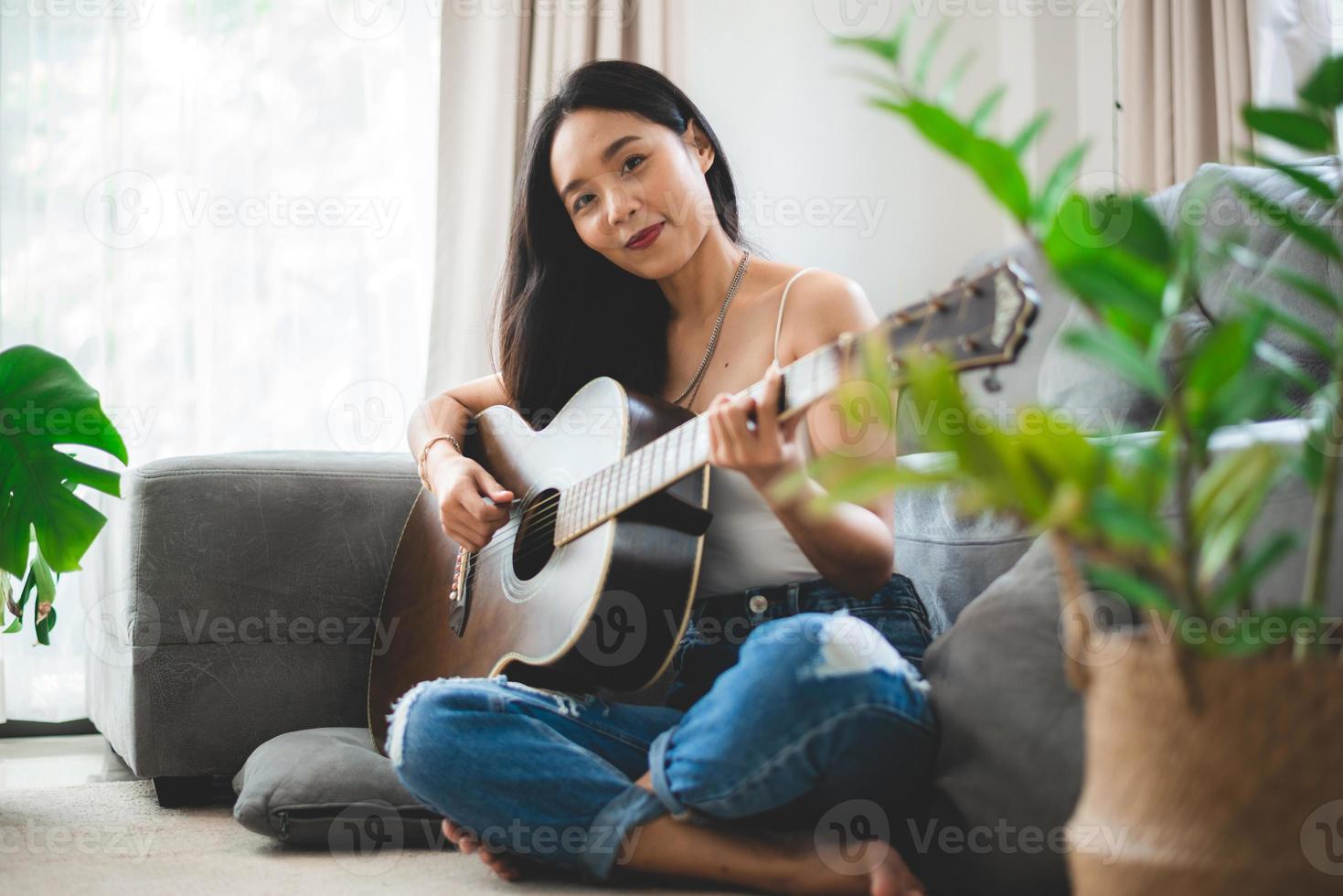 donna asiatica che suona musica con la chitarra a casa, giovane donna chitarrista musicista stile di vita con strumento di arte acustica seduto per suonare e cantare una canzone che fa suono in hobby nella stanza di casa foto