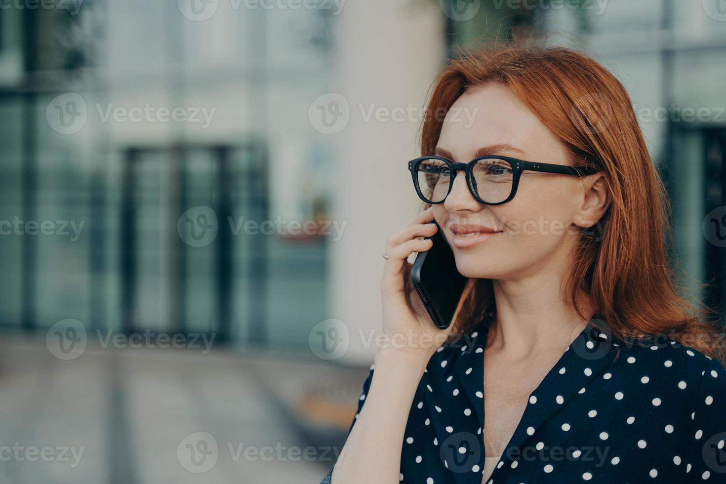 la donna d'affari rossa ha una conversazione telefonica utilizza un moderno gadget cellulare foto