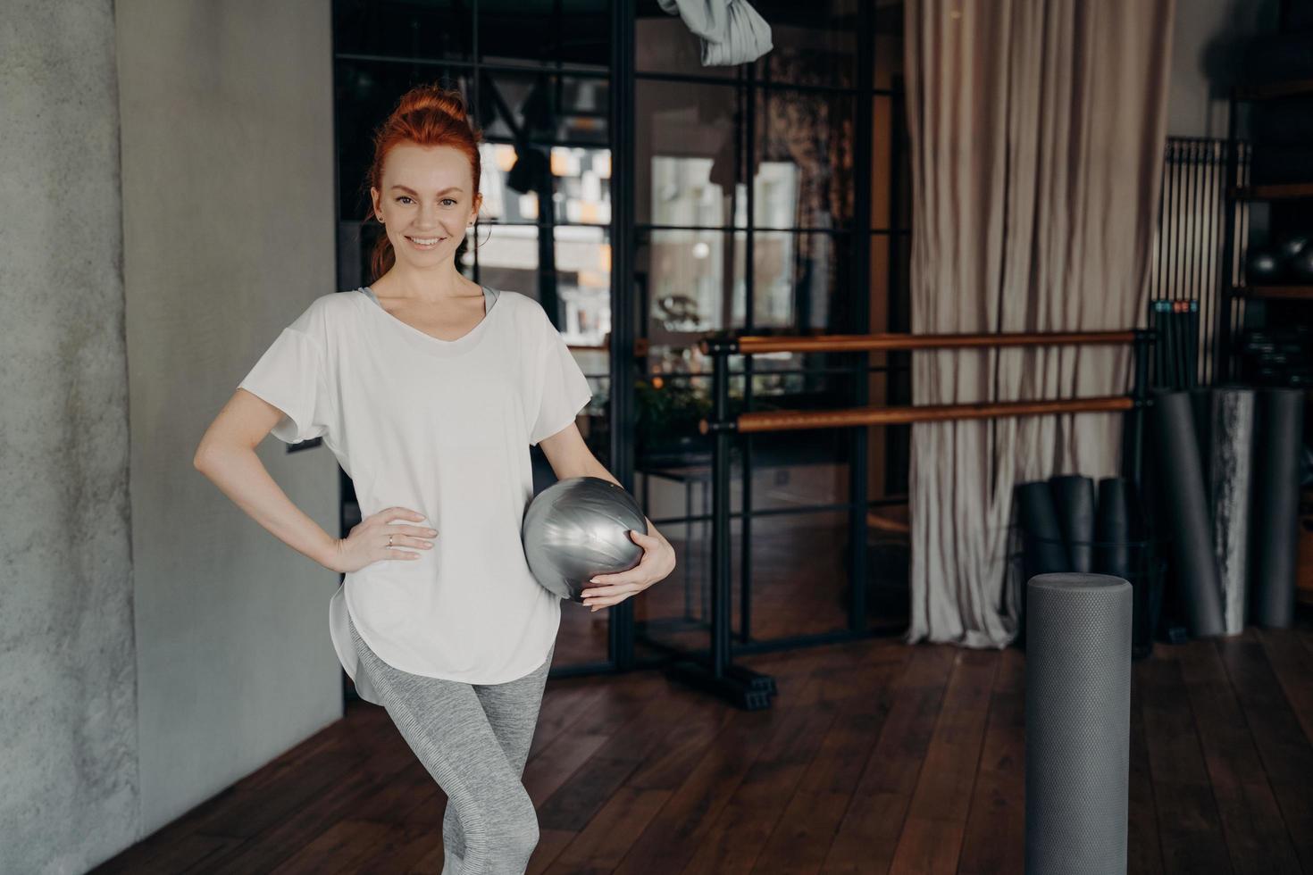 femmina in forma sorridente in posa con palla pilates in palestra foto