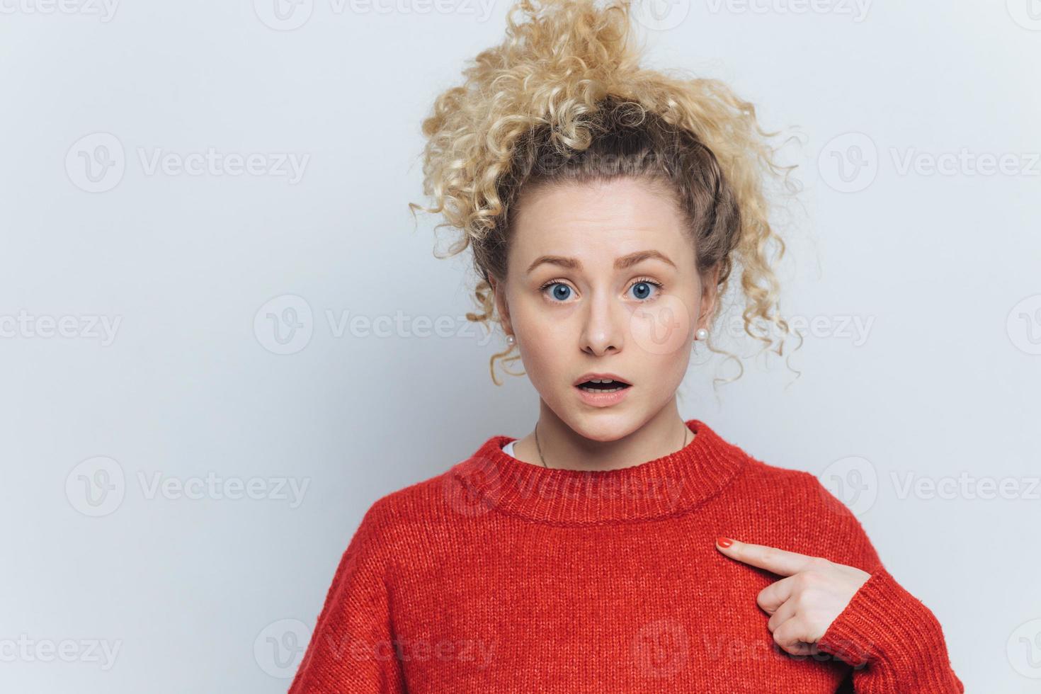 scioccata giovane donna stordita con espressione sorpresa, indica un maglione rosso vuoto, pubblicizza un nuovo vestito, posa su sfondo bianco dello studio con spazio per la copia per il tuo testo promozionale. foto