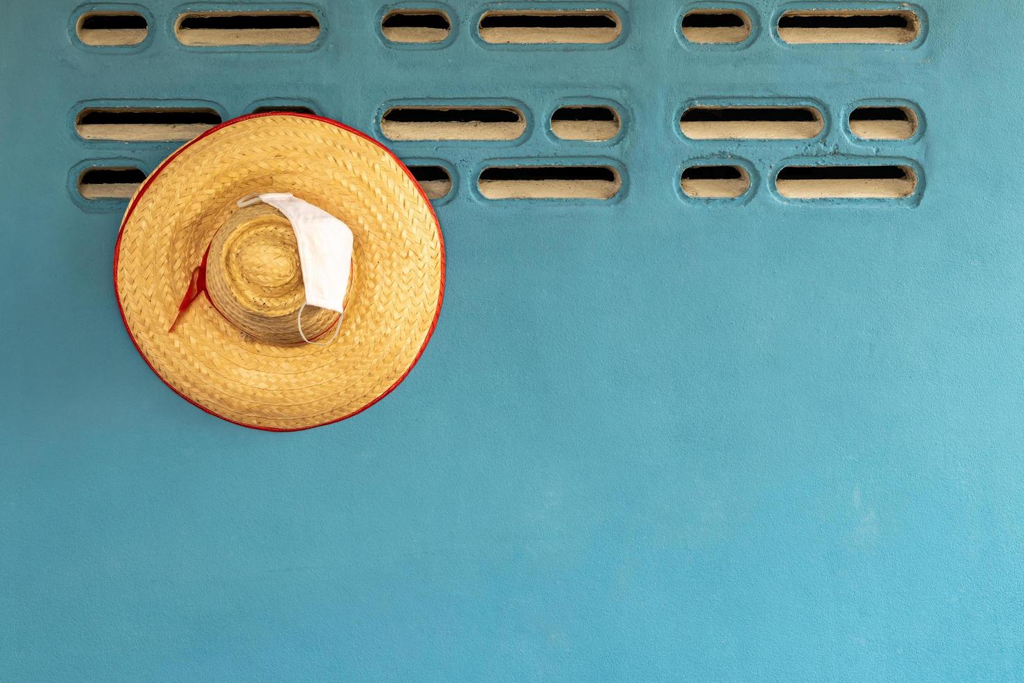 cappello di bambù intrecciato con una maschera appesa a un muro di cemento. foto