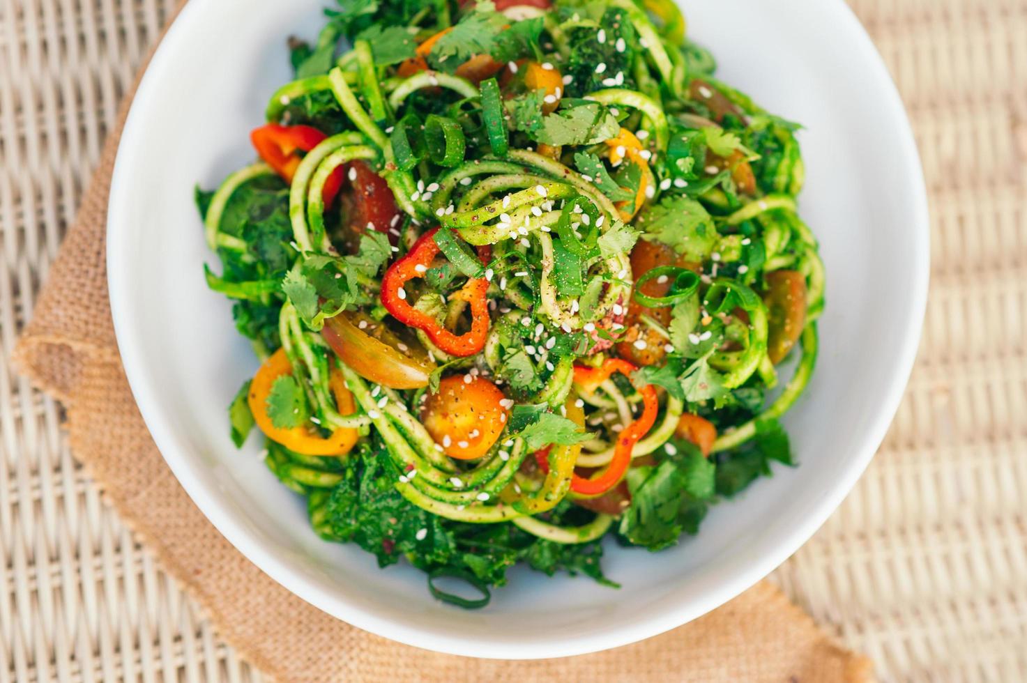 insalata di spaghetti di zucchine con pomodori gialli, peperoncino, cipolla, semi di mare, coriandolo in una ciotola bianca. insalata fresca sul tavolo. piatto di verdure. colpo di vista dall'alto orizzontale foto