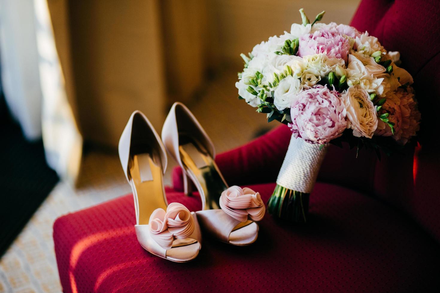 scarpe da sposa e bouquet da sposa con fiori delicati sulla sedia rossa. preparazione del matrimonio. accessori da sposa. scarpe da sposa rosa e bouquet lussureggiante nella stanza delle spose. mattina delle spose. foto del matrimonio