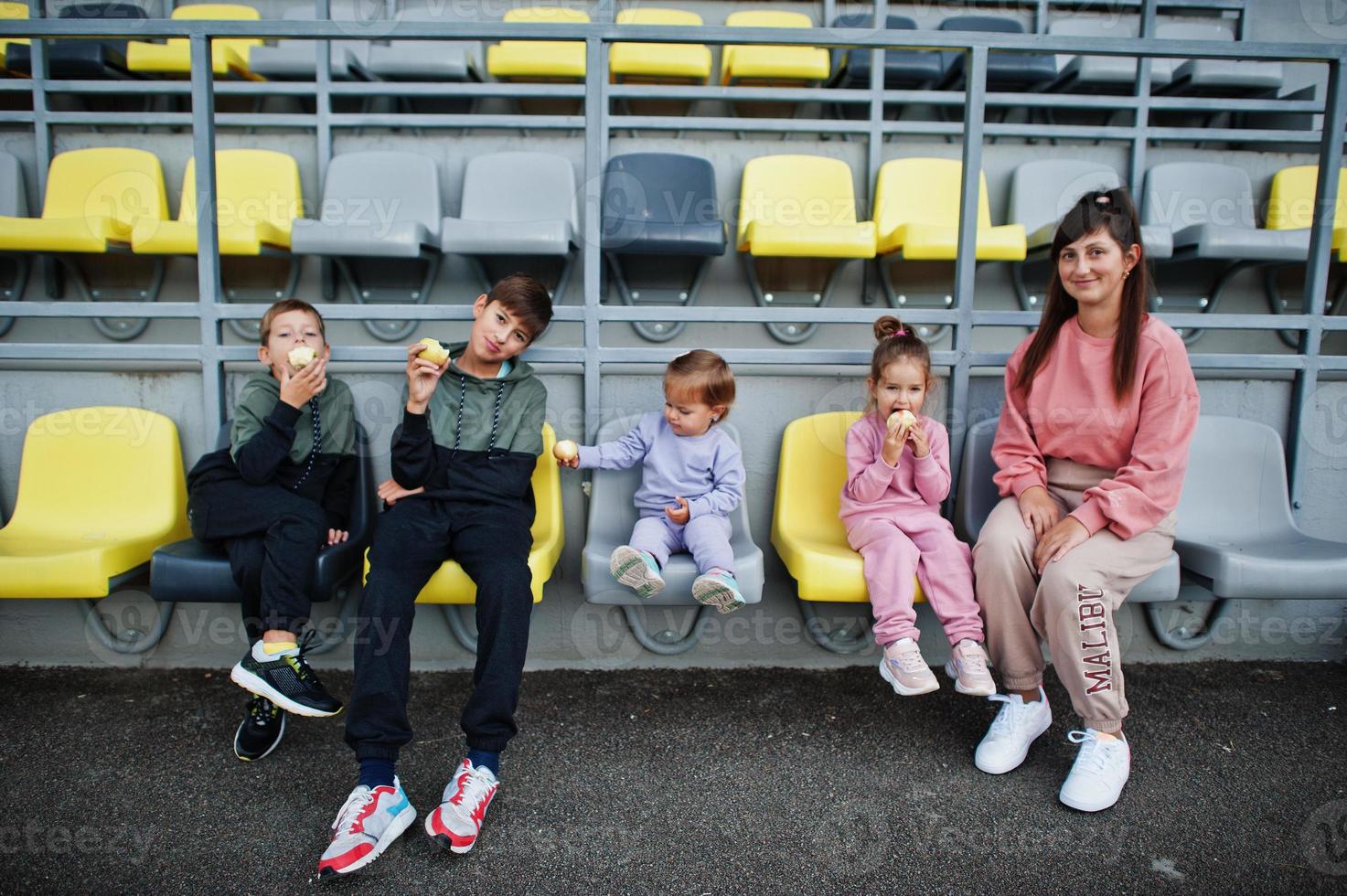 giovane madre alla moda con quattro bambini seduti su sedie allo stadio. la famiglia trascorre il tempo libero all'aperto. foto