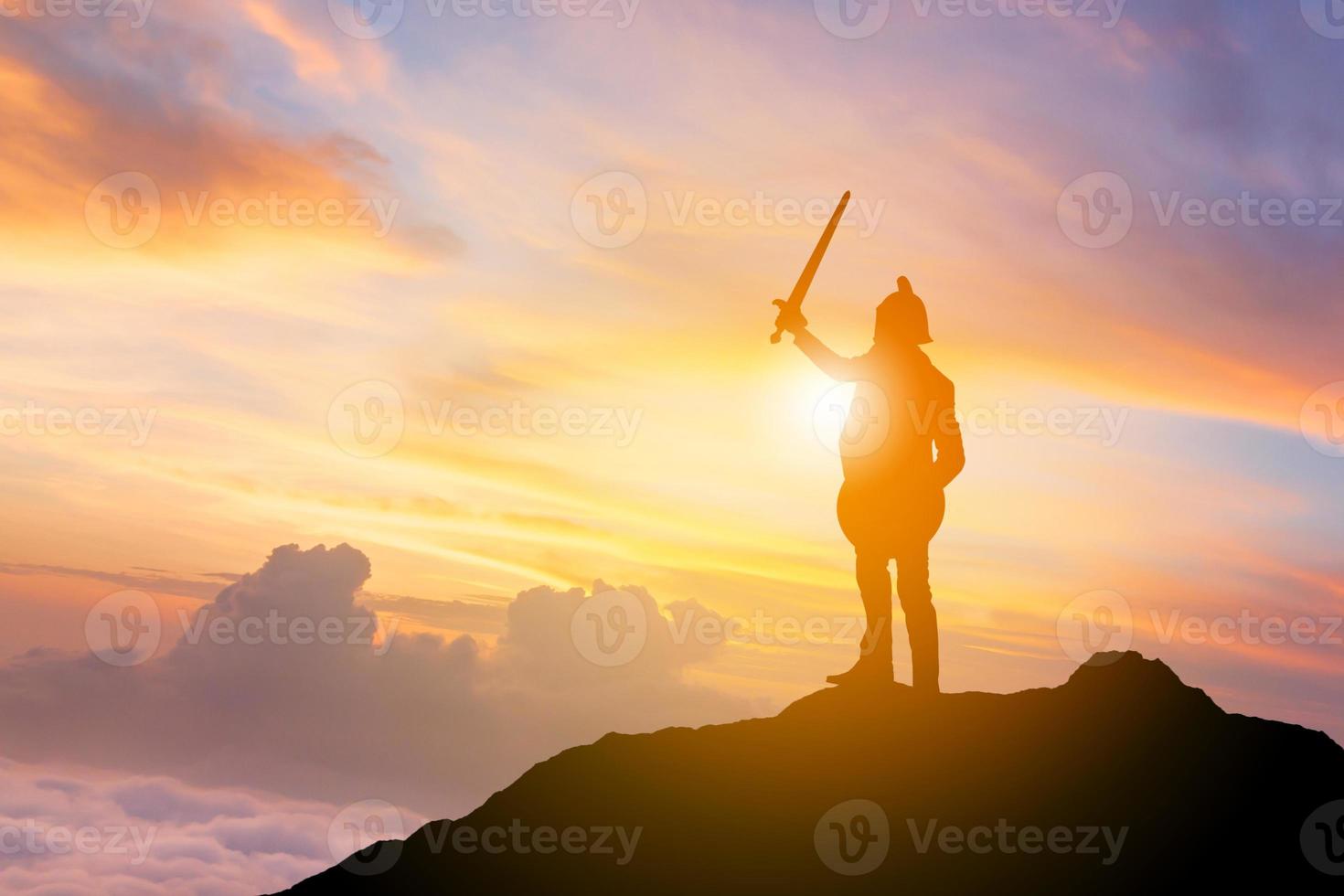 silhouette di uomo d'affari cavaliere spada e scudo sulla cima della montagna sullo sfondo del tramonto, combattendo il concetto di guerriero d'affari. foto