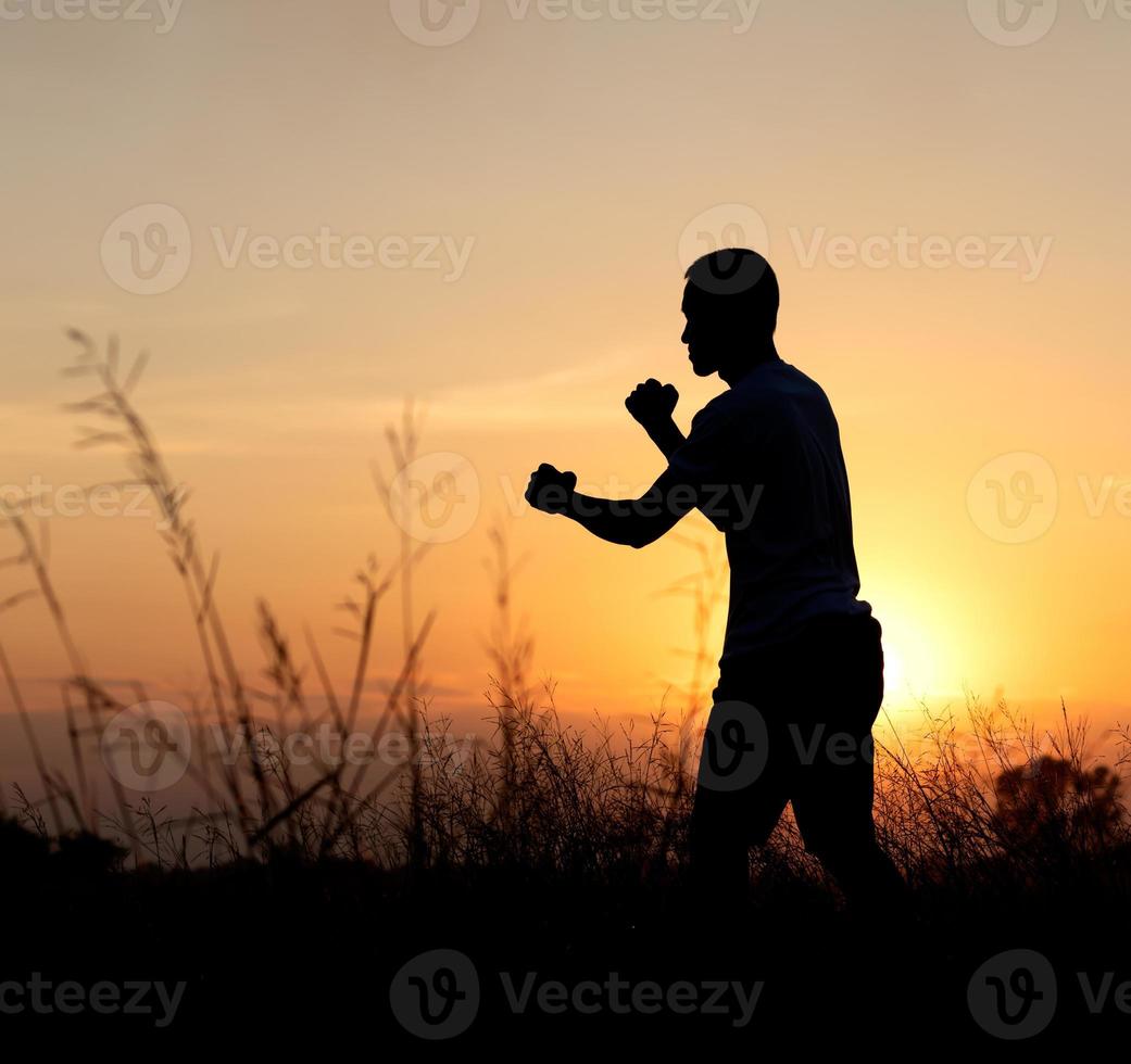 pugile del pugno della siluetta vicino all'erba al tramonto. foto