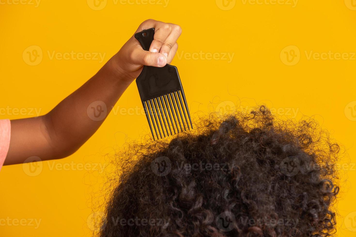 giovani afroamericani che pettinano i capelli isolati. forchetta per pettinare i capelli ricci. sfondo giallo. foto
