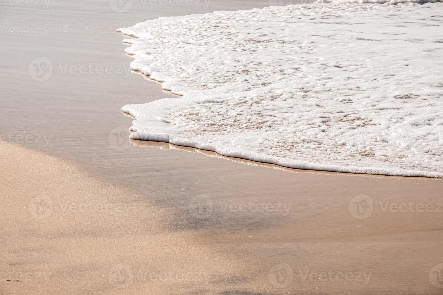 onde morbide con schiuma dell'oceano sullo sfondo della spiaggia sabbiosa foto