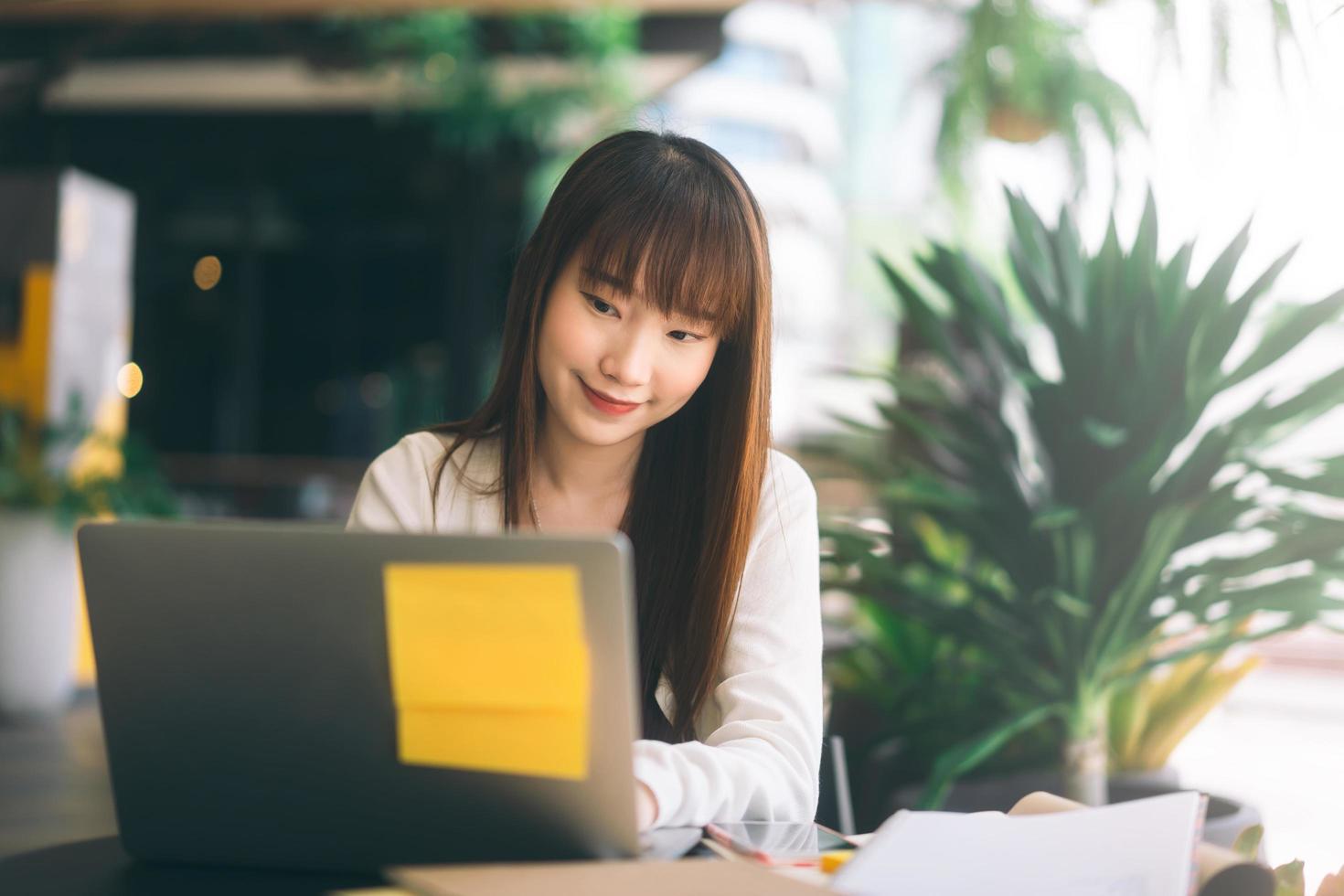 donna asiatica dello studente di college dei giovani adulti che utilizza il computer portatile al caffè. foto