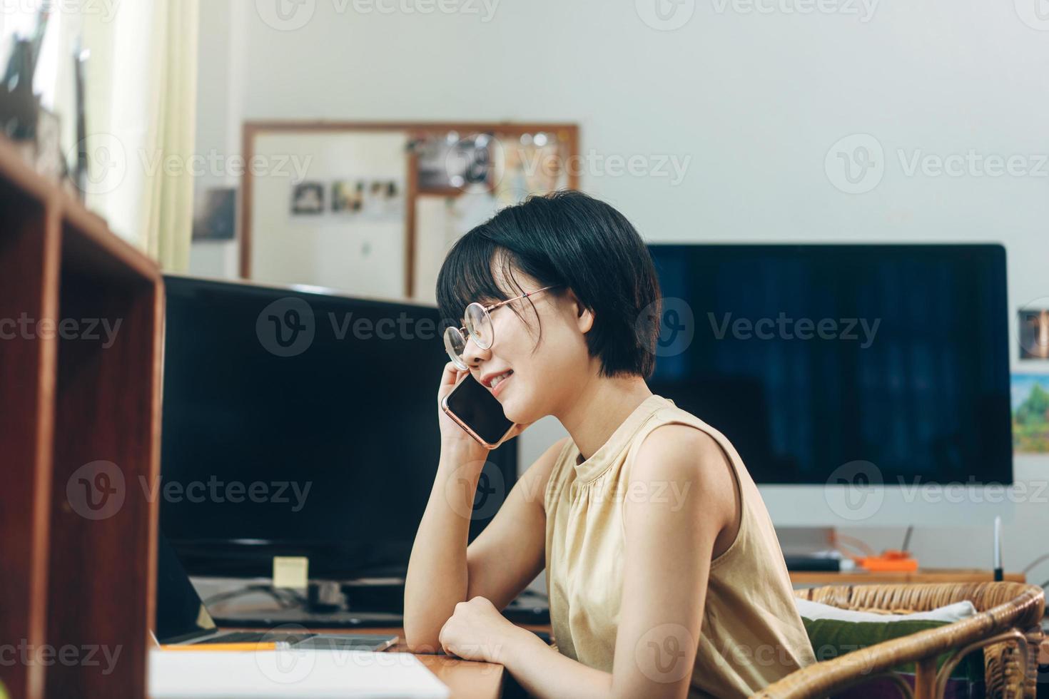 la giovane donna asiatica adulta rimane e lavora dall'ufficio a casa utilizzando lo smartphone al coperto il giorno. foto