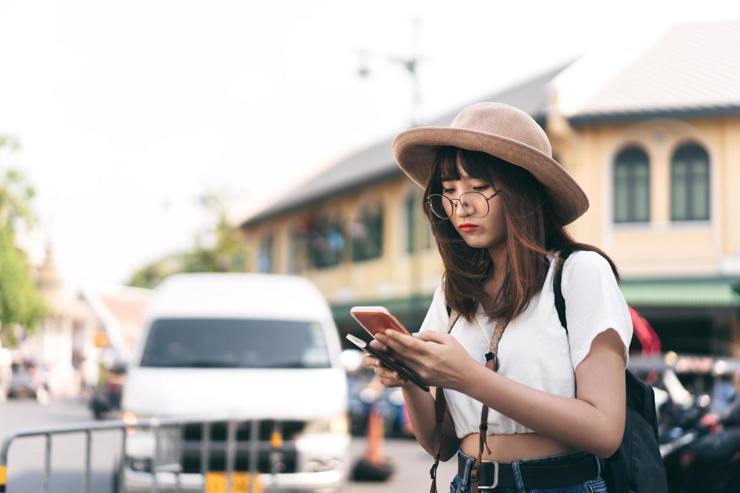 La perdita del viaggiatore della ragazza degli occhiali asiatici durante il viaggio trova la mappa con lo smartphone. foto