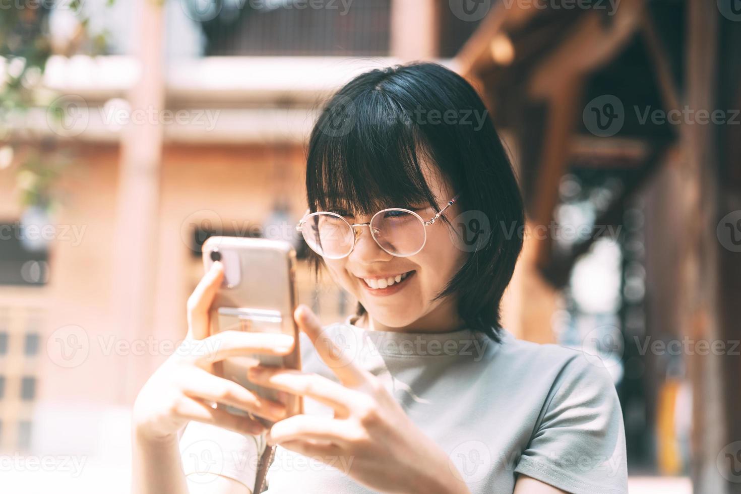 giovane donna asiatica felice adulta indossa occhiali da vista utilizzando il telefono cellulare per i social media. foto