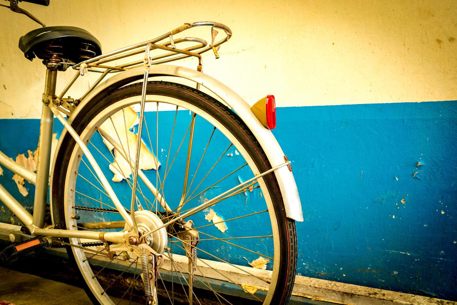 la bici parcheggiata accanto ai vecchi muri di cemento bianco e blu scrostati. foto