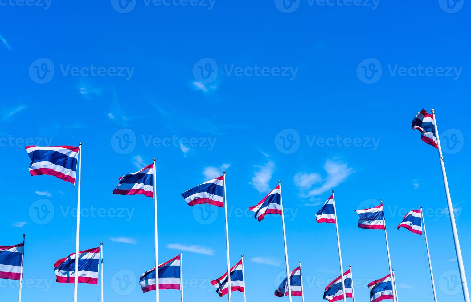 molti della bandiera della Tailandia sventolano sopra il pennone contro il cielo blu. la bandiera tailandese è stata disegnata in cima all'asta della bandiera. tessuto rettangolare di colore rosso, blu e bianco. bandiera nazionale del regno di thailandia. foto