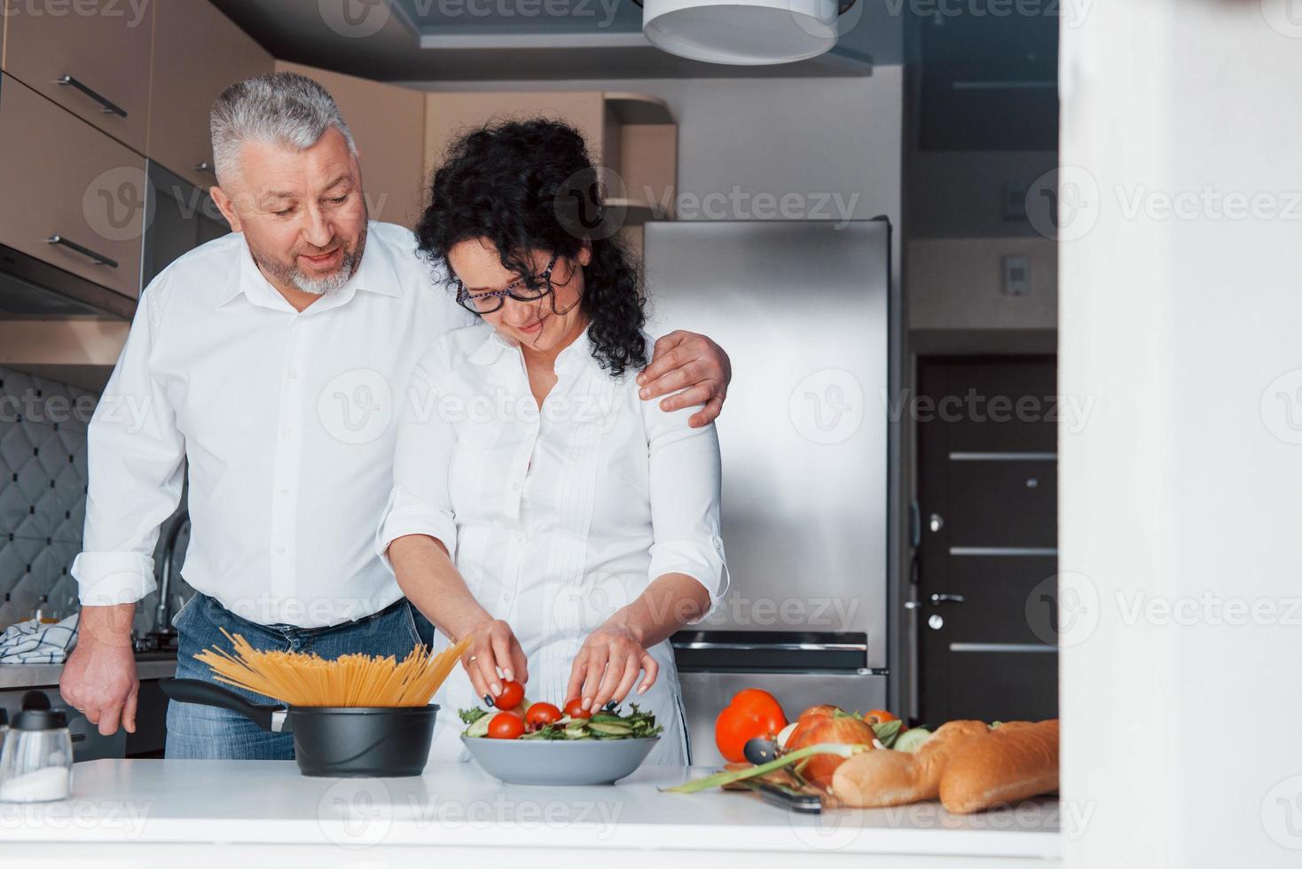 l'amore è come il vino, ogni anno migliora. uomo e sua moglie in camicia bianca che preparano il cibo in cucina usando le verdure foto