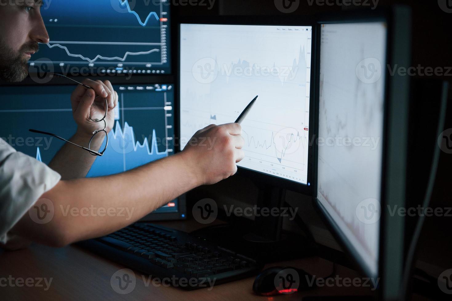 guarda quello. uomo barbuto in camicia bianca lavora in ufficio con più schermi di computer nei grafici indice foto
